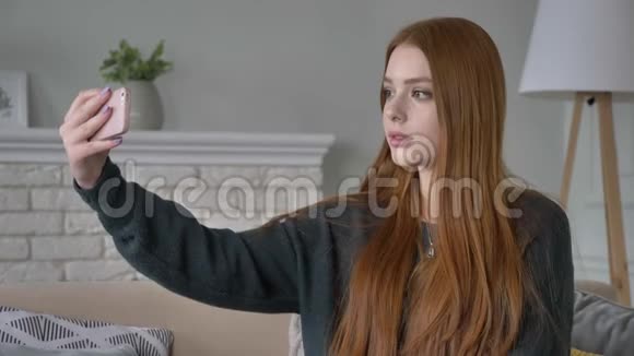 年轻漂亮的红发少女使用智能手机制作自拍家庭舒适的背景60英尺视频的预览图