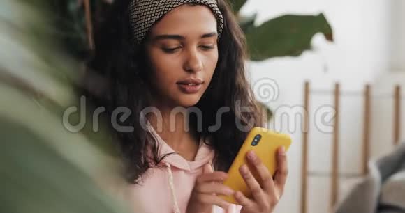 快乐的非裔美国女孩坐在床上在智能手机上和朋友们聊天视频的预览图
