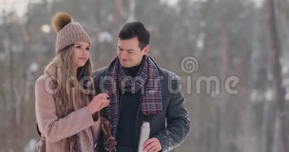 情侣在冬天的森林里喝热水瓶里的茶冬天公园里穿外套的时髦男女视频的预览图