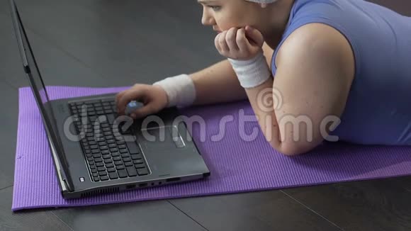 胖女孩躺在笔记本电脑前悲伤地看着屏幕等待信息视频的预览图