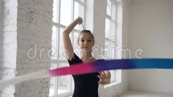 一幅优美的体操肖像在窗户上的白色画室里把彩色丝带旋转在镜头前视频的预览图