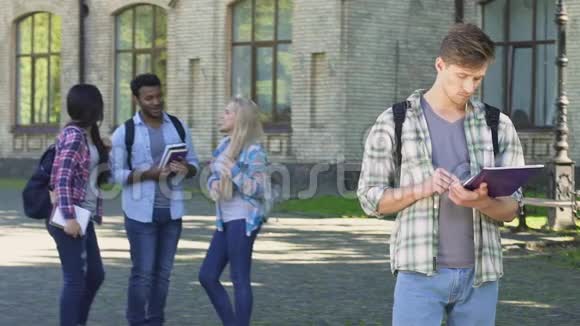 孤独的男学生看着快乐的笑着的同学站在大学附近视频的预览图