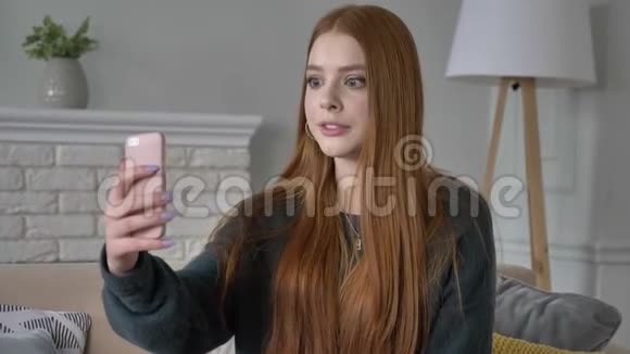 年轻漂亮的红发少女使用智能手机视频聊天家庭舒适的背景60英尺视频的预览图