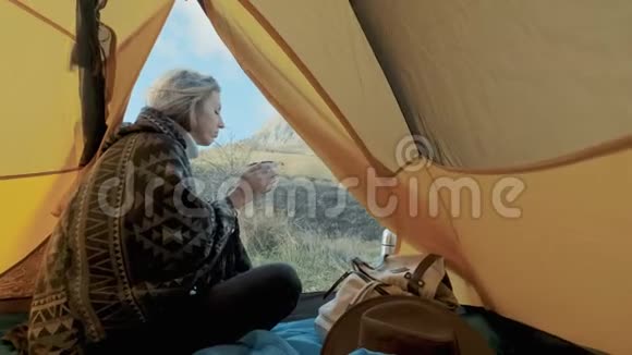 迷人的女孩徒步旅行坐在靠近帐篷入口的山上背景喝咖啡或茶视频的预览图