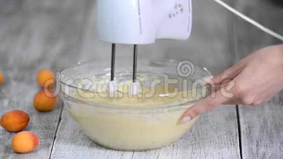 女性用手在木制厨房的碗里用搅拌器搅拌面团做蛋糕视频的预览图