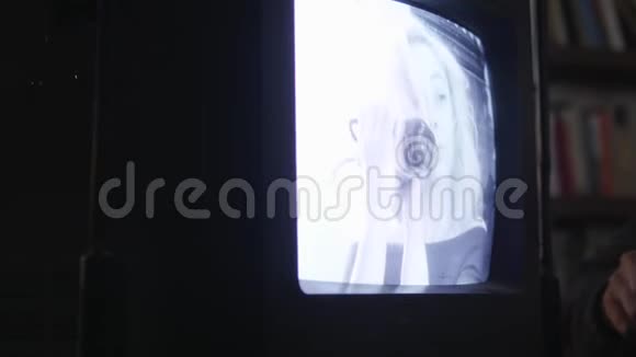 手持安全摄像机的金发女孩出现在旧电视上单色视频的预览图