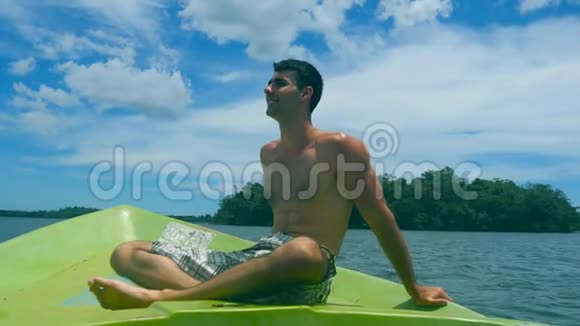 在阳光明媚的日子里年轻的运动员坐在船头眺望美丽的自然景观快乐视频的预览图