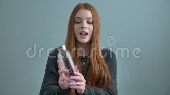 年轻的红发女孩博客写手微笑着对着镜头说话了一个新的购买瓶子换水家的舒适在里面视频的预览图