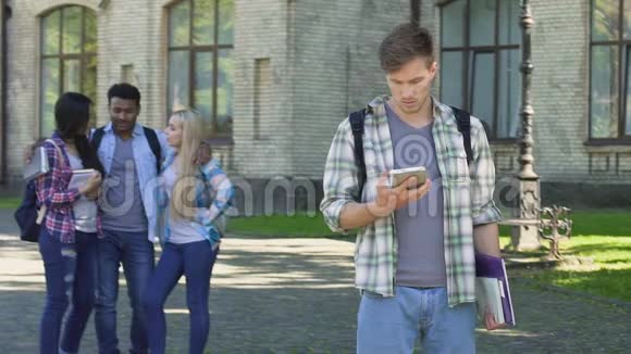 悲伤的男学生在手机上滚动西班牙裔男子与女性调情视频的预览图