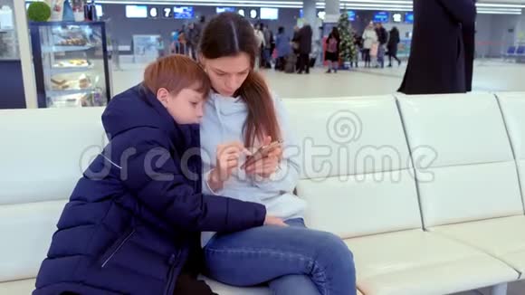 女士带着儿子在机场大厅的手机上在线登记视频的预览图