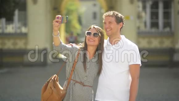 阳光明媚的夏日年轻夫妇在城市广场上用智能手机户外自拍视频的预览图