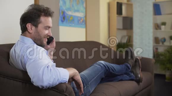 快乐的男人在智能手机上和最好的朋友聊天坐在家里的沙发上视频的预览图