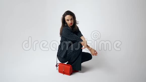 女人模特带着红色的手提包和红色的嘴唇美丽的模特在白色背景的照相馆摆姿势视频的预览图