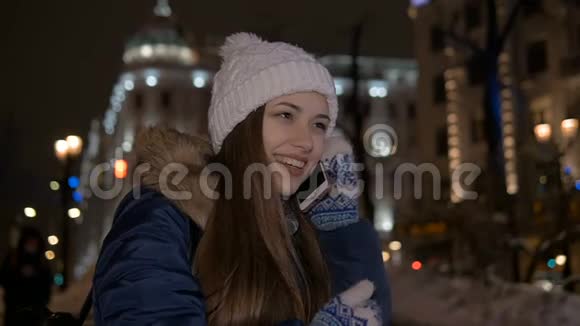 慢动作美丽的女孩微笑着在电话里交谈冬天在街上晚上视频的预览图