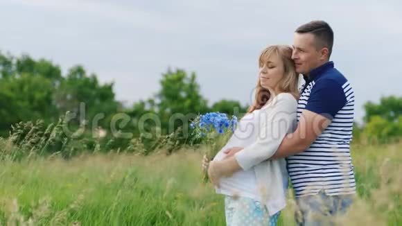 幸福的家庭男人从背后拥抱他怀孕的妻子它在公园或田野里视频的预览图