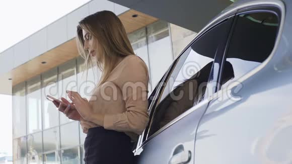 漂亮的女商人在智能手机上和客户聊天站在汽车附近视频的预览图