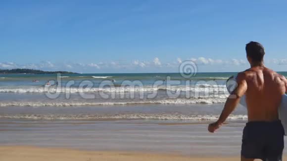 年轻运动员带着冲浪板跑进海洋的后景令人难以辨认的运动型家伙视频的预览图