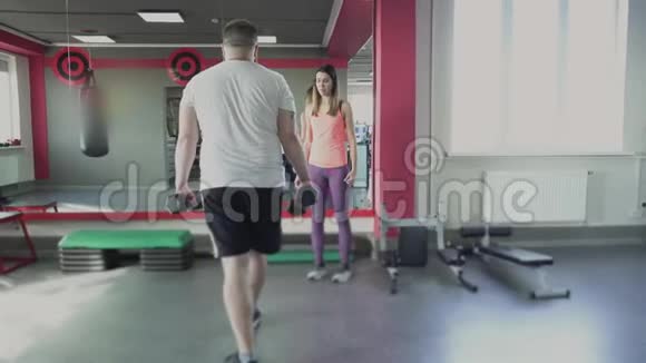 在健身房为男子提供女子教练的个人训练有私人教练的肥胖男人做身体抽搐视频的预览图