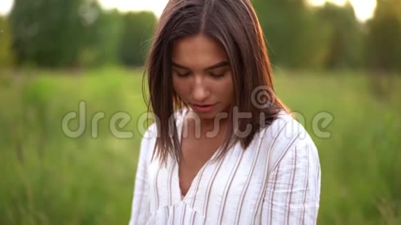 戴着牙套的女人在田野上的夕阳上微笑穿着浪漫的连衣裙飞毛头发视频的预览图