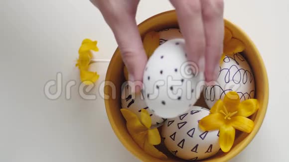 白色背景上的黄色杯子和复活节彩蛋雌性手把一个鸡蛋放进杯子里黄色杯子里的复活节鸡蛋白色视频的预览图