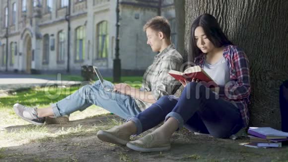 亚洲女孩在树下看书看着男人用笔记本电脑害羞视频的预览图