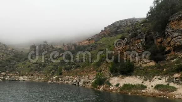 岩石海岸的空中景色山地绿松石湖中的丘陵在多云的天气和雾北部的景观视频的预览图