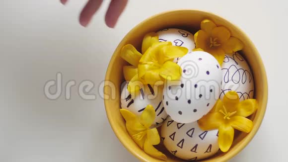 白色背景上的黄色杯子和复活节彩蛋雌性手从桌子上拿出一个带鸡蛋的杯子复活节彩蛋视频的预览图