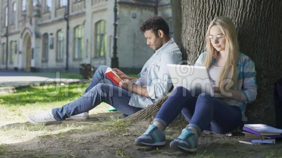 男人带着书女人带着笔记本电脑在树下互相看着微笑着视频的预览图