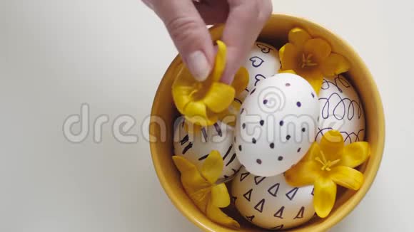 白色背景上的黄色杯子和复活节彩蛋雌性手把一朵黄色的花放在复活节的鸡蛋上复活节彩蛋视频的预览图