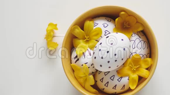 白色背景上的黄色杯子和复活节彩蛋雌性手从杯子里拿出一个鸡蛋黄杯中的复活节彩蛋视频的预览图
