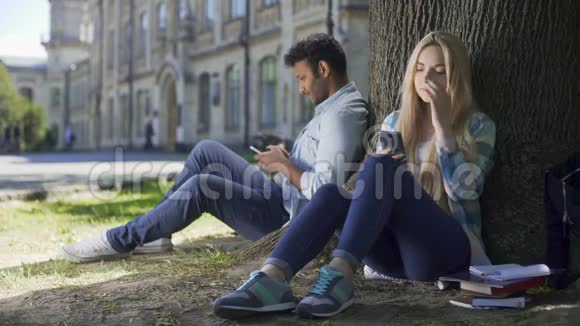 男女陌生人坐在树下互相交替地看着视频的预览图