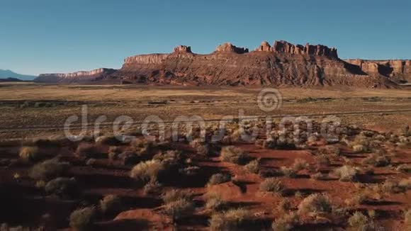 无人机低飞上方干燥的沙漠景观与平坦的山脉接近银色小型货车附近的小公路道路视频的预览图