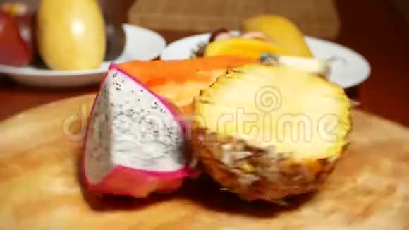 餐桌上的异国水果火龙果木瓜菠萝切碎旋转在一个切割板上视频的预览图