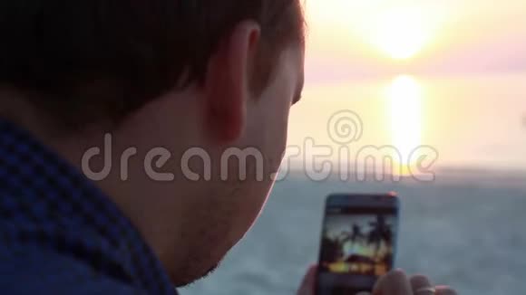 在美丽的夕阳下帅哥在海滩上的酒吧休息时使用手机有人在网上发布照片视频的预览图