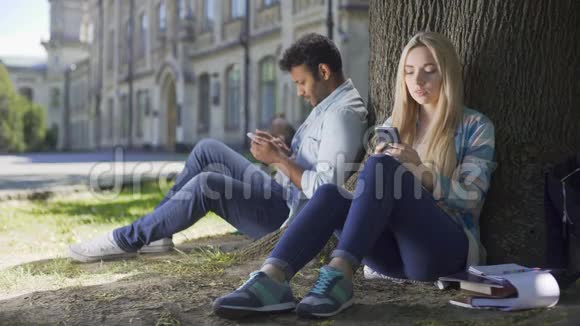 男女陌生人坐在树下用手机女孩沉重地叹息视频的预览图