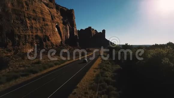 无人机照相机跟随汽车行驶在小沙漠公路道路附近惊人的陡峭峡谷山脊日落在美国视频的预览图