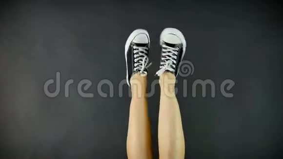经典黑白运动鞋中的女性腿腿是上升和倾斜从侧面到侧面黑色背景视频的预览图