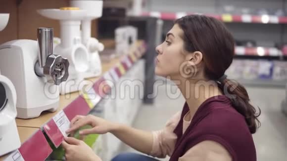 年轻女性消费者比较电器肉磨床在电器商店寻找完美厨具的价格视频的预览图