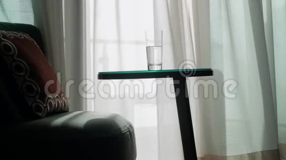 一张舒适的扶手椅和一张桌子窗户上透明的窗帘背景下有一杯水视频的预览图
