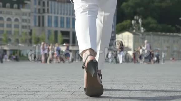 女性腿白色裤子和凉鞋走在城市沥青上舒适的鞋子视频的预览图