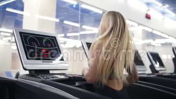 年轻迷人的白种人金发碧眼身穿黑色运动服穿着斯洛莫体育馆里的跑步机视频的预览图
