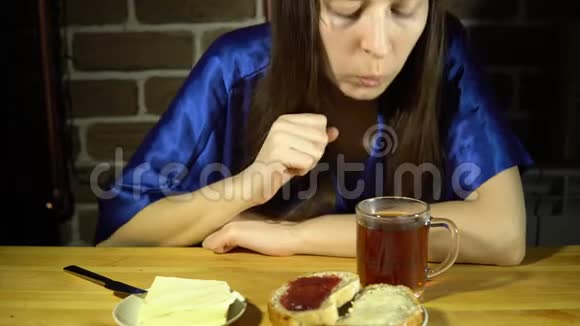 年轻的女人吃面包和果酱喝热茶视频的预览图