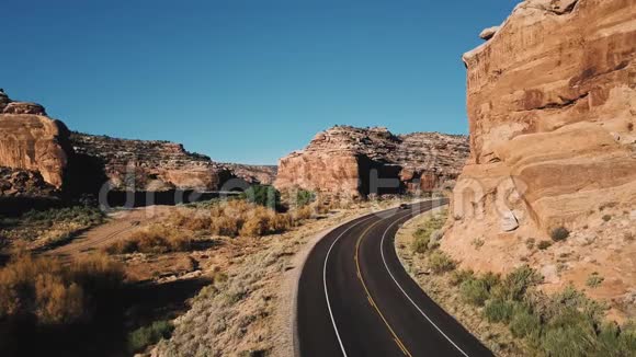 在亚利桑那州一个阳光明媚的日子里汽车在沙漠公路上的小路上经过静态无人机摄像机在惊人的巨大悬崖之间视频的预览图