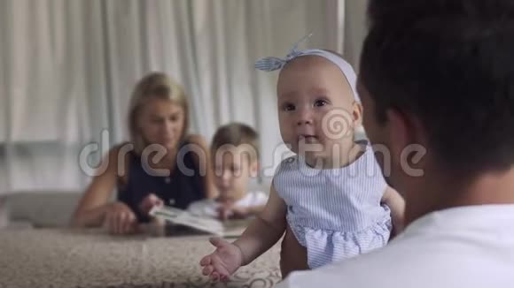 戴着蝴蝶结的小可爱女孩从爸爸手里看镜头视频的预览图