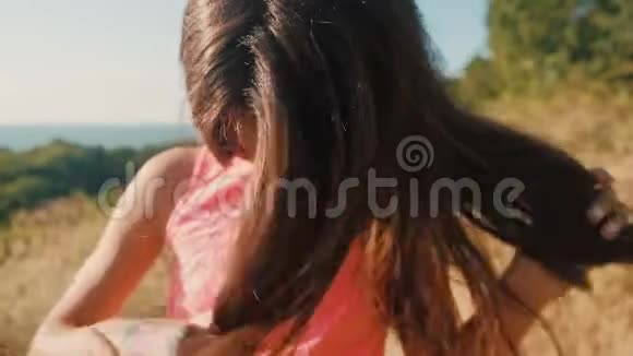 穿着粉红色裙子的女孩在户外晒太阳玩着她棕色的长发视频的预览图