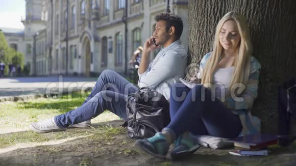 年轻男女坐在树下男人打电话女孩写字视频的预览图