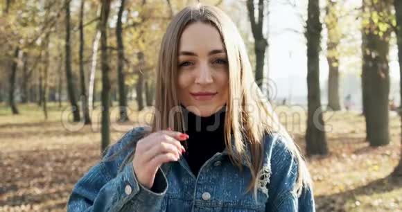 年轻迷人的女性的肖像她微笑着看着秋天公园的相机开心的漂亮女人视频的预览图