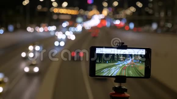 智能手机安装在三脚架上他们在美丽的灯光背景下拍摄汽车运动的照片视频的预览图