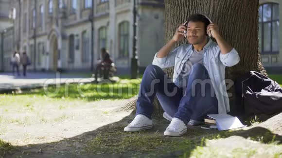 年轻人戴着耳机听着音乐坐在树下赞叹不已视频的预览图