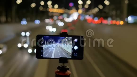 智能手机安装在三脚架上他们在一个美丽的灯光背景下拍摄视频车流量视频的预览图
